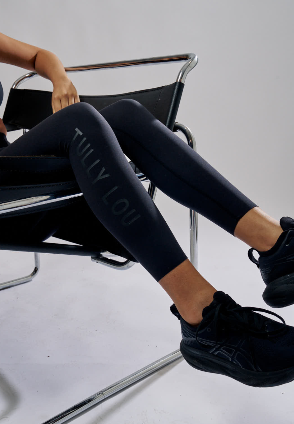 Person wearing black leggings with 'Tully Lou' branding, sitting on a chair.