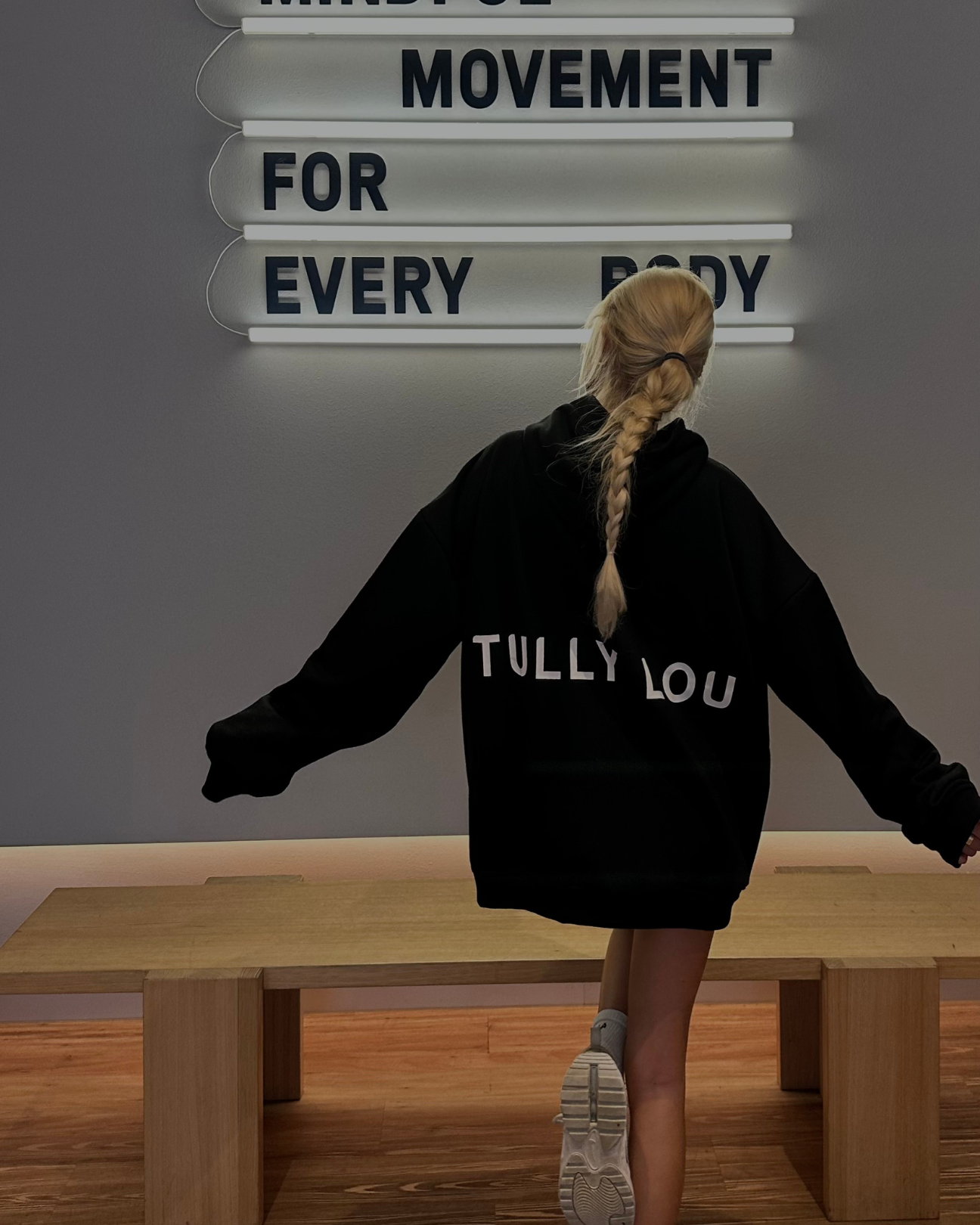 Morgan Riddle workout pilates in oversized black Tully Lou hoodie in front of a movement sign