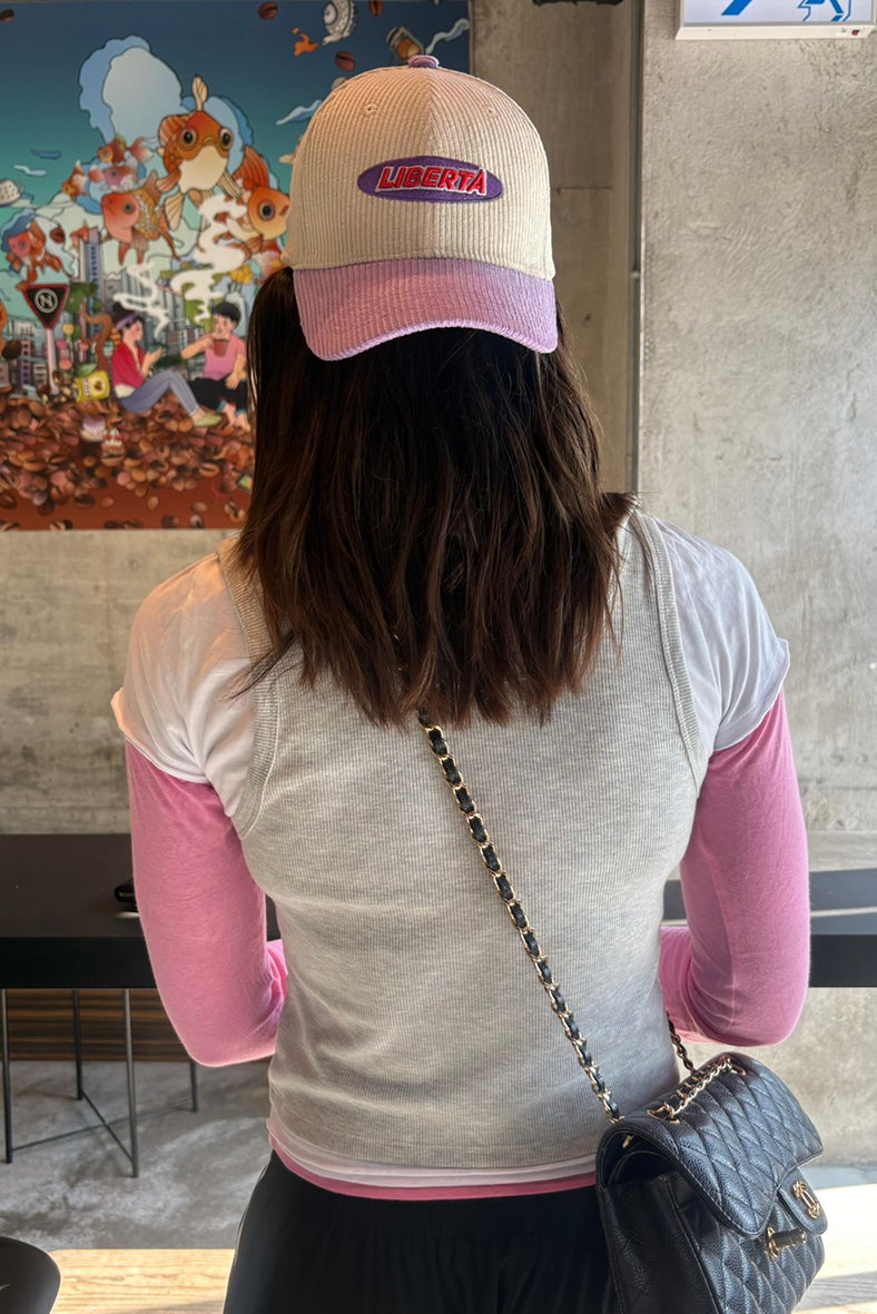 Person wearing a cap with 'Liberta' logo, standing indoors with a colorful mural in the background.