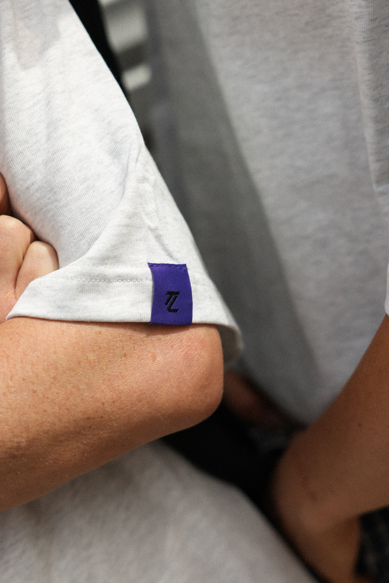 Close-up of a person wearing a white shirt with a purple and blue logo on the sleeve.