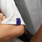 Close-up of a person wearing a white shirt with a purple and blue logo on the sleeve.