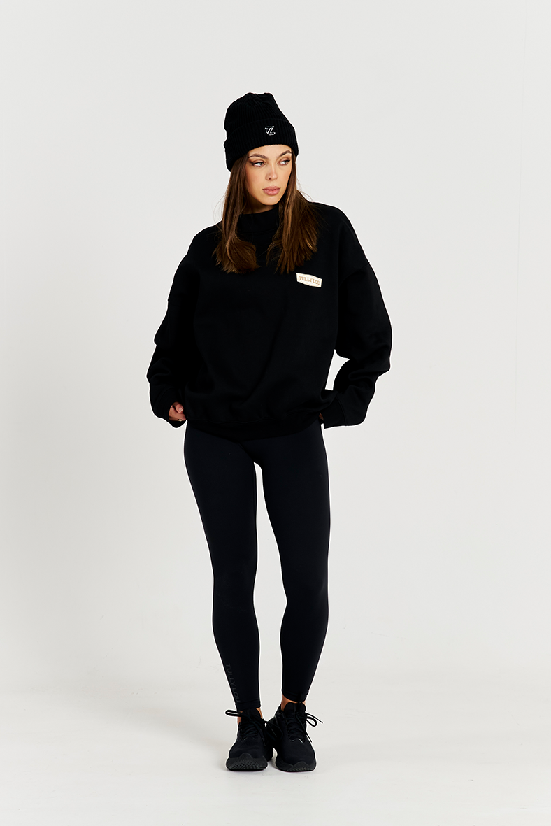 model standing with black leggings with black round neck jumper and black beanie 