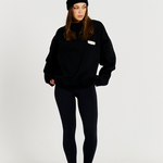 model standing with black leggings with black round neck jumper and black beanie 