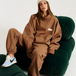 Model on green couch wearing mocha tracksuit heavy fleece set with cream beanie 