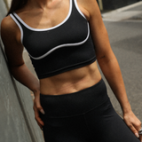 Woman wearing a black sports bra and leggings leaning against a wall.