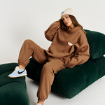 model on green couch wearing brown tracksuit set with cream beanie on and blue and brown sneakers
