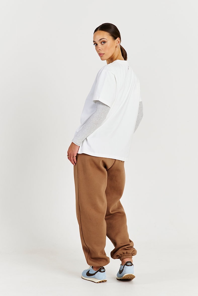 back of white tee layered with long sleeve top and brown track pants 