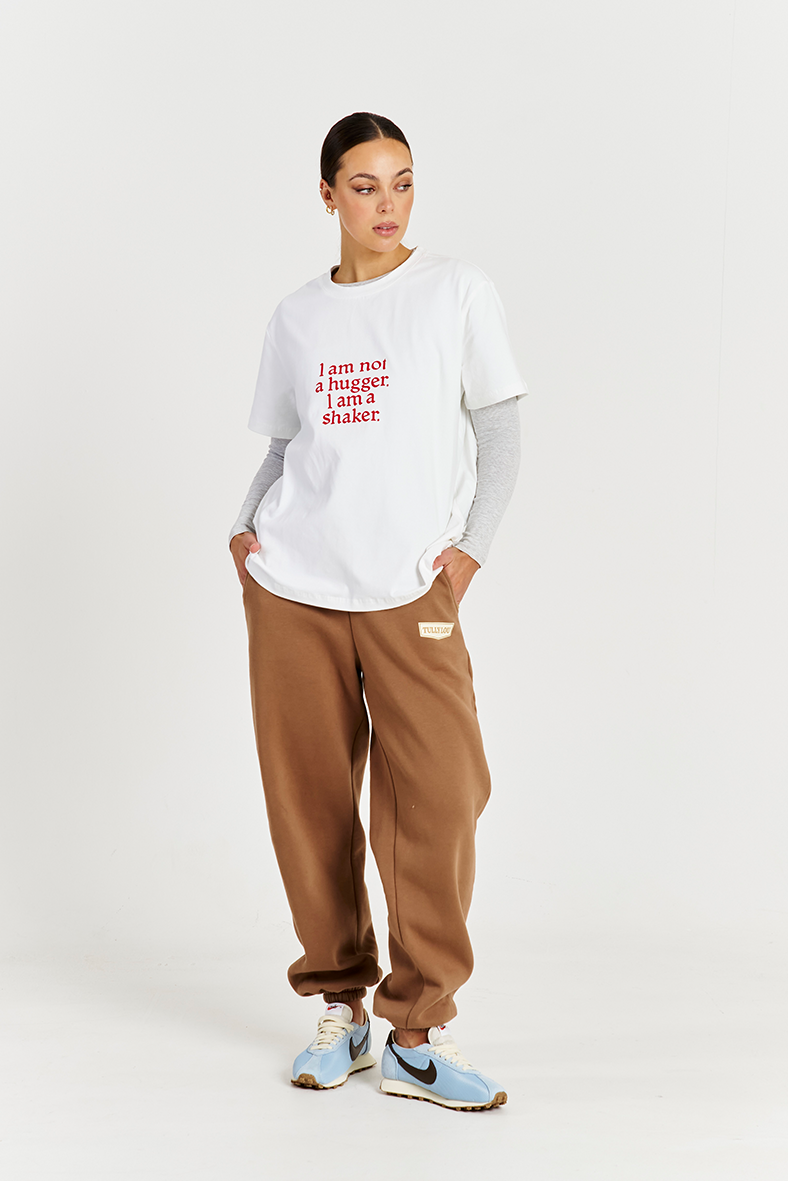 model wearing white tee with red text logo and brown track pants 
