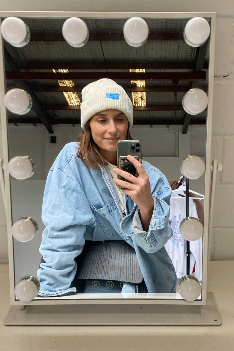 white beanie with blue logo on model posing in a mirror