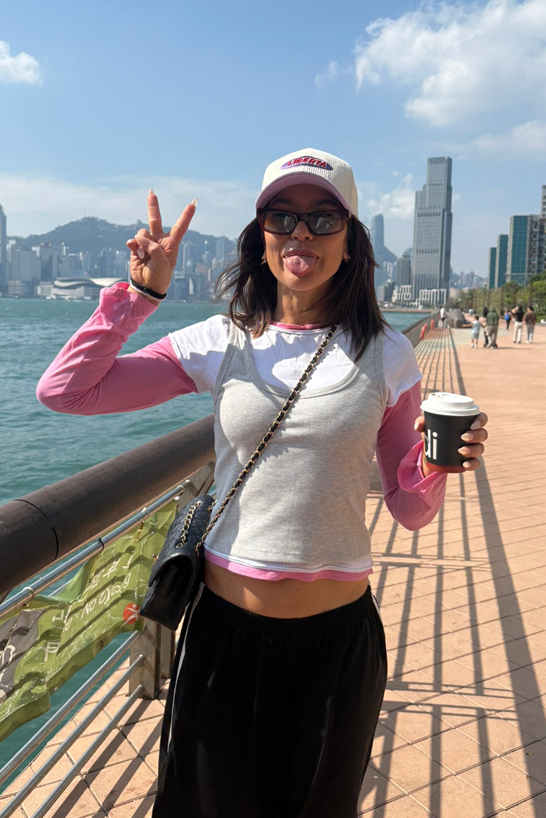 Woman on a bridge with a cityscape and water in the background, holding a coffee cup.