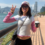 Woman on a bridge with a cityscape and water in the background, holding a coffee cup.