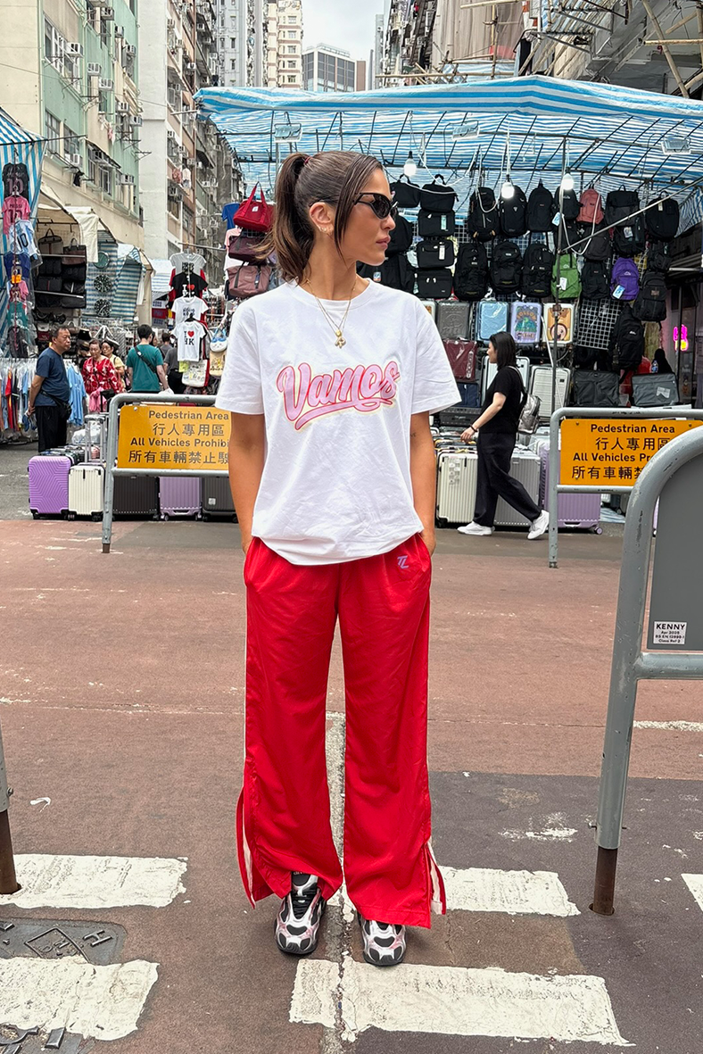 Person wearing a white t-shirt with pink text and red pants standing on a street.