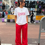 Person wearing a white t-shirt with pink text and red pants standing on a street.