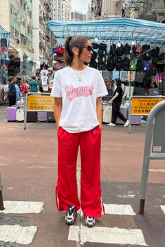 Person wearing a white t-shirt with pink text and red pants standing on a street.